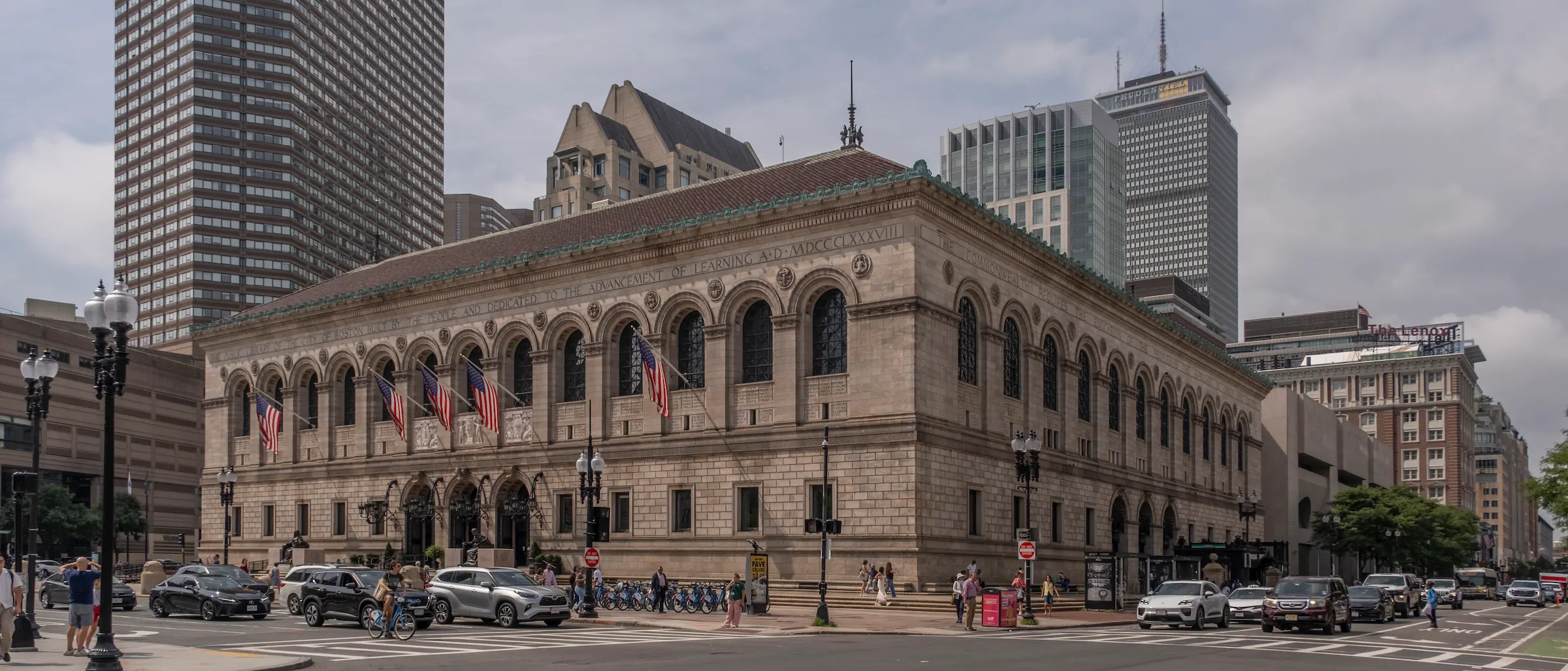 The Boston Public Library's McKim building at Copley Square, flags out over the arched windows and traffic passing on Boylston Street